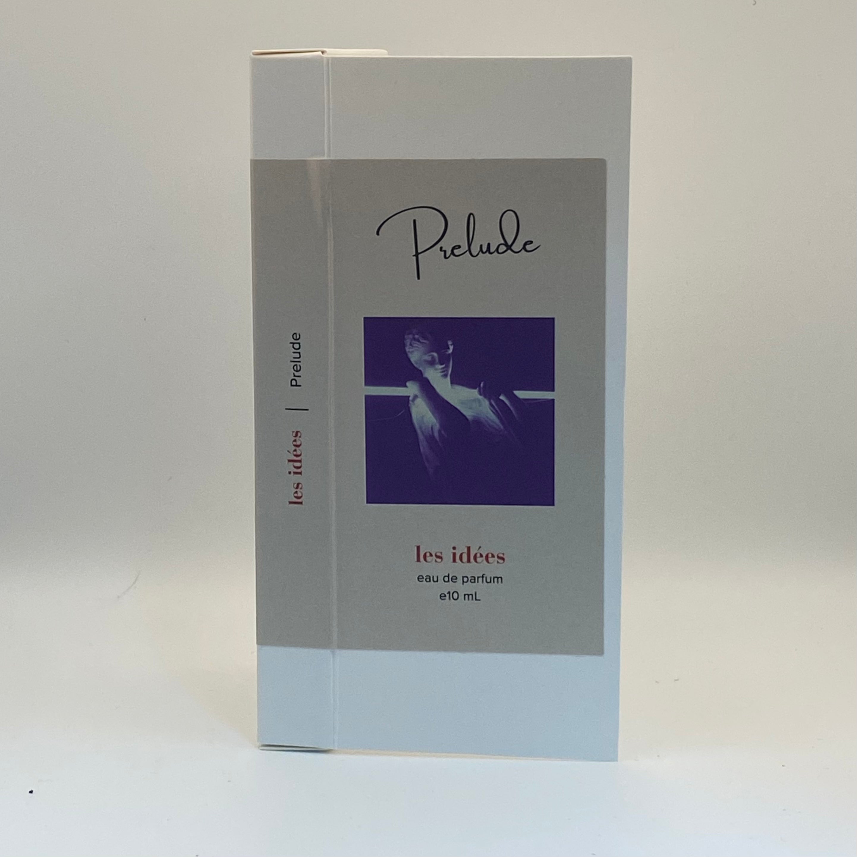 Perfume box labeled 'Prelude' with a purple square featuring a face on a white background